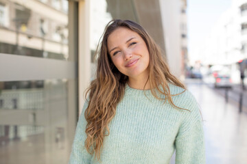 pretty hispanic woman smiling cheerfully and casually, taking hand to head with a positive, happy and confident look