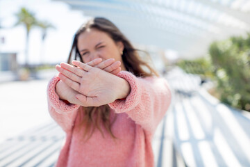 pretty hispanic woman covering face with hand and putting other hand up front to stop camera,...