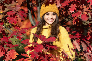 positive teen child in hat at autumn leaves on natural background