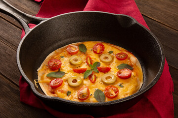 Cheese pizza pan with cherry tomatoes and olives inside a iron skillet pan in cropped front view