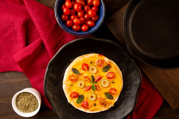 Homemade Pizza pan with tomatoes, basil and olives in a black plate in top view