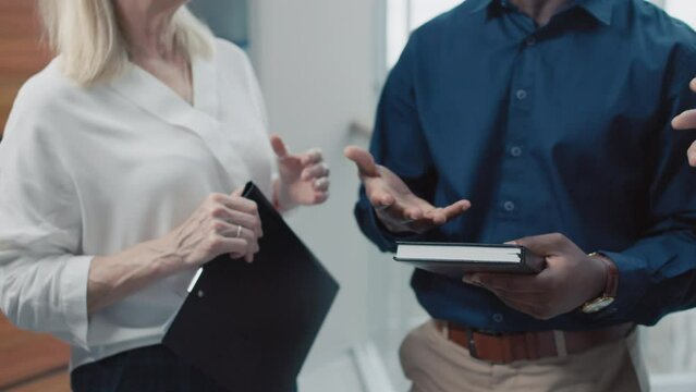 Cropped shot of office workers holding planners and folders while standing and talking to each other indoorsCropped shot of office workers holding planners and folders while standing and talking to ea