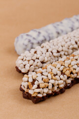 Chocolate bars coated with corn cereals, peanuts pieces and white icing on beige background.