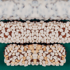 Sweet chocolate bars coated with corn cereals, peanuts pieces and  white icing on green background. Top view.