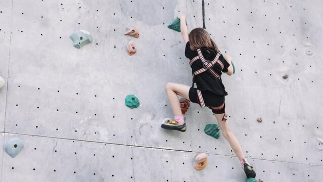 Little girl, child climbing upwards artificial wall with rock. Outdoor training. Choosing correct path. Concept of extreme sport, hobby, active lifestyle, health and strength