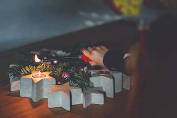 Hand of child lighting a candle on advent wreath on Christmas eve or first advent. Tradtional...