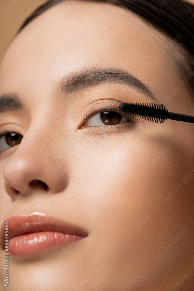 Wall mural Close up view of asian woman with natural visage posing near mascara applicator isolated on beige