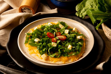 Arugula pizza pan with cheese and cherry tomatoes inside handmade ceramic plate above a wooden table in tow view