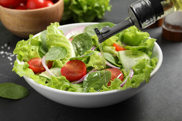 Pouring oil into delicious vegetable salad on grey table, closeup