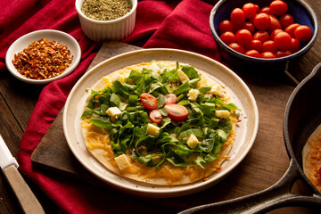 Arugula pizza pan with cheese and cherry tomatoes inside handmade ceramic plate above a wooden table in tow view