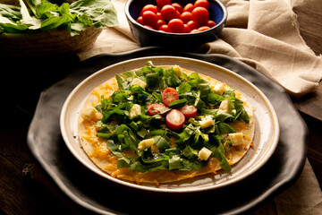 Arugula pizza pan with cheese and cherry tomatoes inside handmade ceramic plate above a wooden table in tow view
