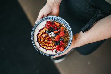Person holding healthy breakfast acai bowl with red fruit and granola