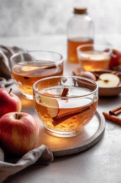 Two glass mugs of spiced apple tea with cinnamon and apple slices. Vertical, side view