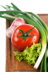fresh vegetables - tomato, green onion, garlic and lettuce leaf on a wooden board isolated on white background