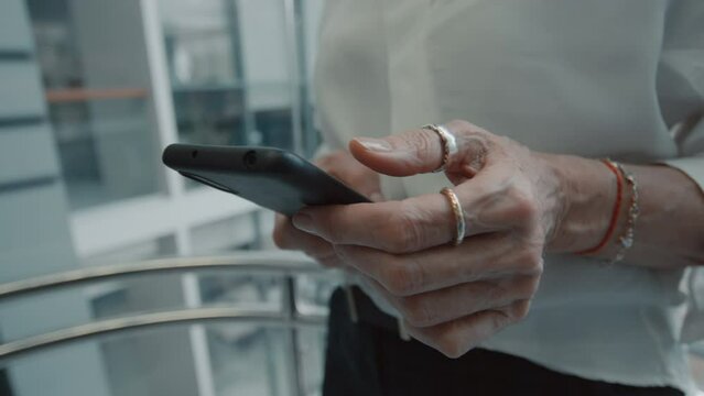 Close up of female hands of office worker using smartphone while going up in elevator in modern business center