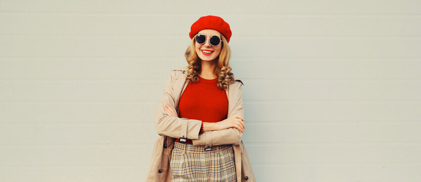 Autumn style outfit, stylish happy smiling young woman model wearing red french beret hat, jacket and round sunglasses on gray background
