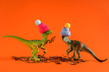 Two green dinosaurs playing with autumn leaves.