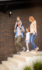 Family with a mother, father, son and daughter walking by the wall of brick house