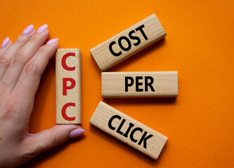 CPC - Cost Per Click symbol. Concept word AGM on wooden cubes. Businessman hand. Beautiful orange...