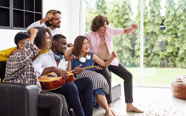 Group of diverse friends or people wearing casual clothes, relax smiling with happiness, party celebration, sitting in living room at cozy home, playing guitar and singing. Birthday, New Year Concept.