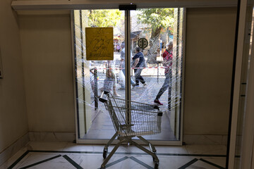 Broken glass of the front door of the supermarket. Modern fashionable glass armored door in a web...