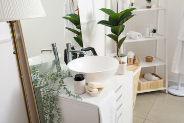Fototapeta na wymiar Soap bars, dispenser, houseplant and sink bowl on chest of drawers in bathroom