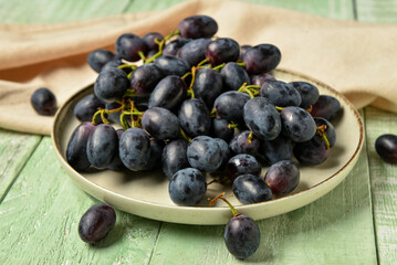Plate with sweet black grapes on green wooden background