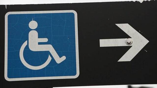 handicap sign blue logo with white arrow on its right pointing right on black rectangle horizontal sign on post with sky in background, tight shot