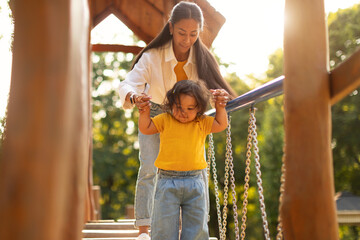 Japanese Mom and Toddler Walking on Swinging Bridge On Playground