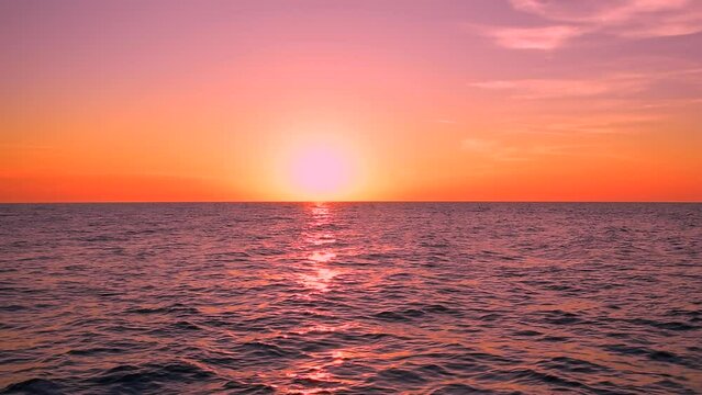 Beautiful sea waves with shiny reflection of purple and pink sunset light. Colorful clouds on the red sky, calm horizon scene view, sunny day, sun, beach, outdoor, mid shot, slow motion. ProRes 422 HQ