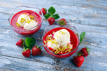 Traditionelle gefrorene Erdbeersuppe mit Vanilleeis und gehackte Pistazien serviert als Nahaufnahme auf einem rustikalen Holz Board mit Textfreiraum