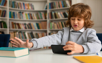 Reluctance to learn. Caucasian schoolboy using phone and pushing the book away, playing game or watching videos online