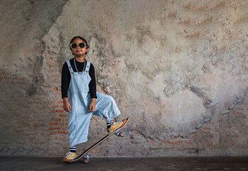 Portrait of happy cute little African boy wearing glasses standing and posing while playing on a skateboard with having fun in the skateboard stadium.