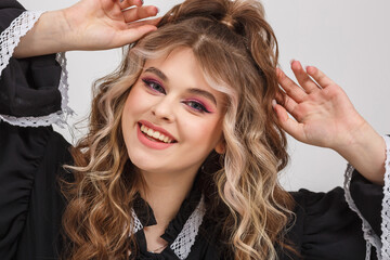 Fototapeta premium young girl in black school dress poses as doll on white background in studio