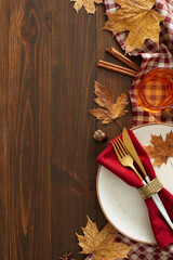 Embrace the warmth of autumn at your table. Top view vertical photo of plate, cutlery, tablecloth, glass, cinnamon, acorn, dry leaves on wooden background with empty space for promo or message