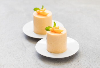 Vegan dessert. Apricot cream pudding, Panna Cotta cylindrical shape, decorated with small fresh apricot slices. On a plate. Light gray background