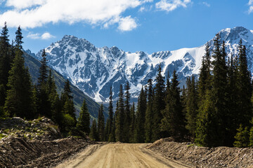 Road in Barskoon gorge, with snow-covered mountains and forest, to Barskoon pass. Kyrgyzstan