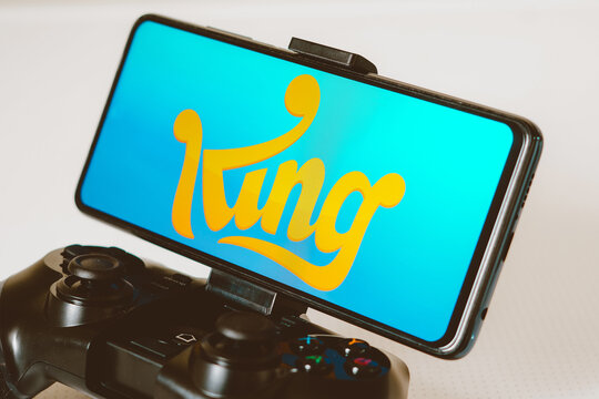 August 14, 2023, Brazil. In this photo illustration, the King Digital Entertainment logo displayed on a smartphone screen, connected to a gaming joystick.