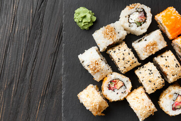 Set of various sushi rolls on a black slate plate, close-up.