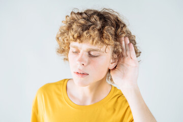 Curious curly-haired guy eavesdropping with his palm to his ear. Close up portrait.