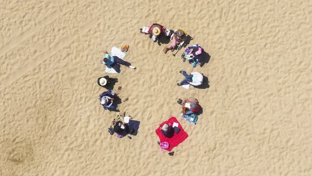 Top view of friends sitting on the beach, Santa Monica, Los Angeles, California, USA. Group of people talking together outdoors. Overhead shot of women and men relaxing on the sandy shore, 4k footage 