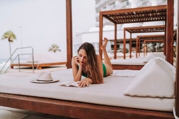 Chica joven delgada en cama balinesa descansando y leyendo tranquilamente 