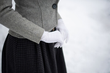 Lady's waist closeup in retro style. Vintage gray wool jacket, heavy plaid wool skirt and white gloves. Warm suit for winter walking, light snowy background. Edwardian fashion, history reconstruction