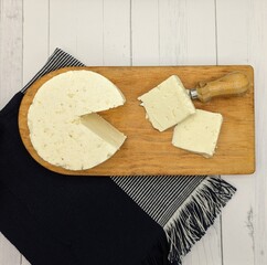 Sliced panela cheese and cutter on wooden dish. White wooden table with blue tablecloth
