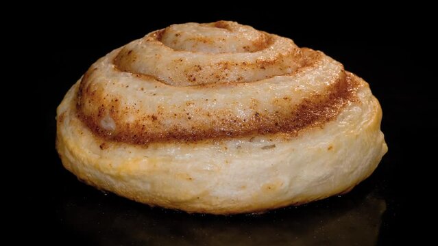 Timelapse - one cinnamon bun baking and rising on tray in electric oven - close up view, black background. Homemade bakery, food, cooking, pastry and time lapse concept