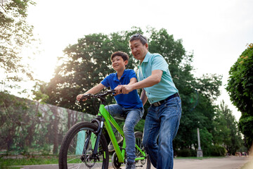 asian old father and son ride bikes together in the park, korean senior and grandpa are active with...