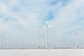 Scenic landscape view of white snowy frosty field and big modern wind turbine mill farm against beautiful blue clouds blue sky. All season clean green renewable sustainable energy generation concept
