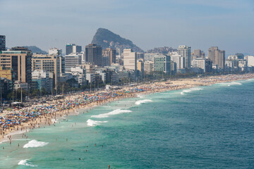 Leblon and Ipanema beach in Rio de Janeiro, Brazil. Sunny day with blue sky and many people on the beach. Plenty of umbrellas on the sand. Weekend. Turquoise and clear sea