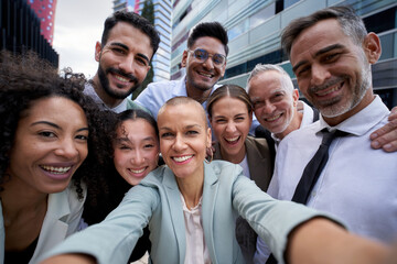 Selfie of happy business people taking photo with a phone. Multiracial teamwork taking a portrait of big group of colleagues. Corporative lifestyle of a diverse office workers in a financial center