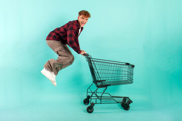 young crazy guy shopper jumps and rejoices with shopping cart from supermarket